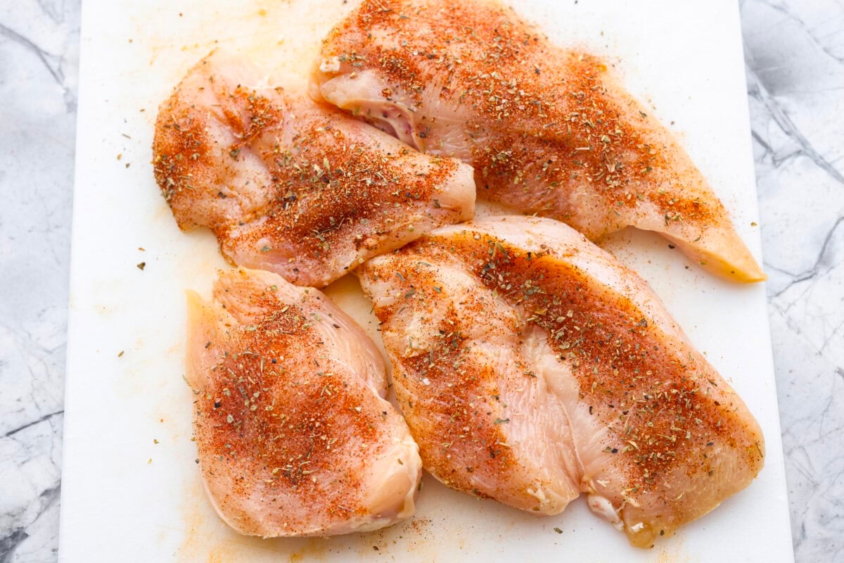 If you’re looking to save time, keep your sanity, and hit your protein goals, these chicken and rice meal prep bowls have you covered. They're flavorful, filling, and give you that “I’ve got my life together” feeling. Seasoned chicken on a cutting board.