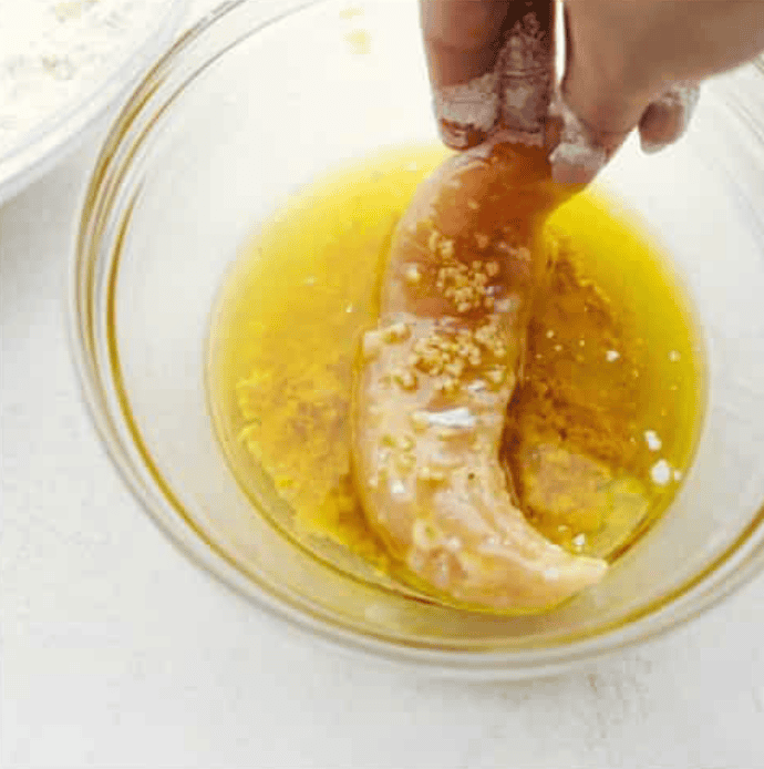 These air fryer chicken tenders are a lifesaver on crazy weeknights. Crispy, cheesy, and full of flavorโplus they cook up fast and my kidsย actuallyย ask for seconds. Total win! Someone dipping the flour coated chicken in butter.