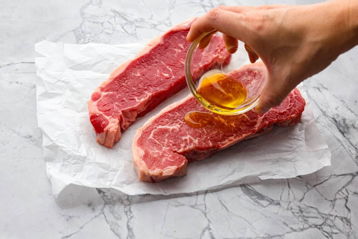 My Air Fryer Steak is a favorite around here for a reason! Itโs perfectly seared, super juicy, and so full of flavorโitโs my go-to way to make steak! Someone pouring oil over the raw steaks.