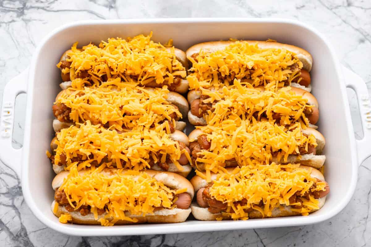 These Baked Chili Cheese Dogs are dangerously good. We’re talking soft buns, hearty chili, and ooey gooey cheese. They’re quick, messy (in the best way), and totally delicious! Chili and cheese evenly distributed over the hot dogs in hot dog buns.