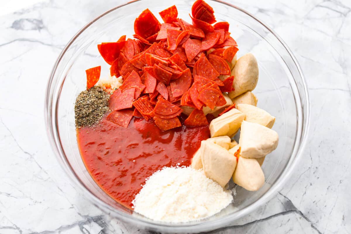 Bubble Pizza is what you make when you want something cozy, cheesy, and easy. Think pizza meets pull-apart bread with zero rolling, stretching, or takeout guilt. Cut up biscuit pieces with pepperoni, sauce, seasoning and cheese in a bowl.