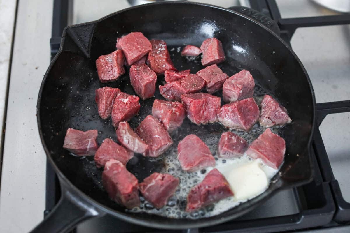 Get ready to obsess! These Garlic Butter Herb Steak Bites with Potatoes are juicy, buttery, and downright irresistible. Easy to make, crazy delicious, and pure comfort in every bite! Cubed steak pieces searing in a skillet with butter melting next to them.