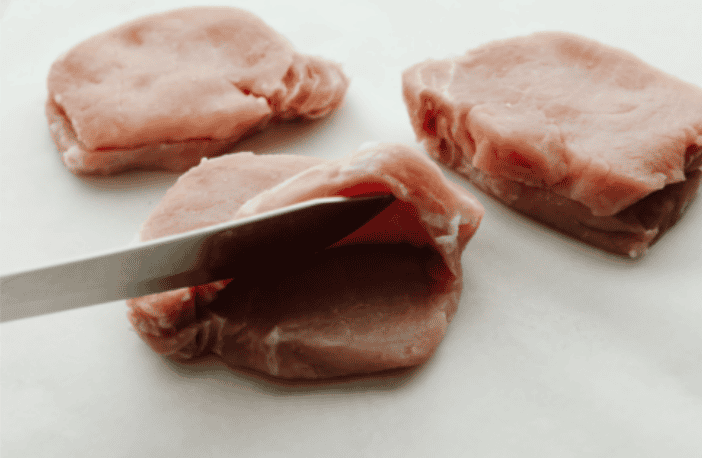 Stuffed pork chops sound fancy, but they’re super easy and budget-friendly. I’ll show you how to keep the pork chops moist and stuffed with gooey, cheesy deliciousness! Process shot of someone slicing a pork chop with a sharp knife.
