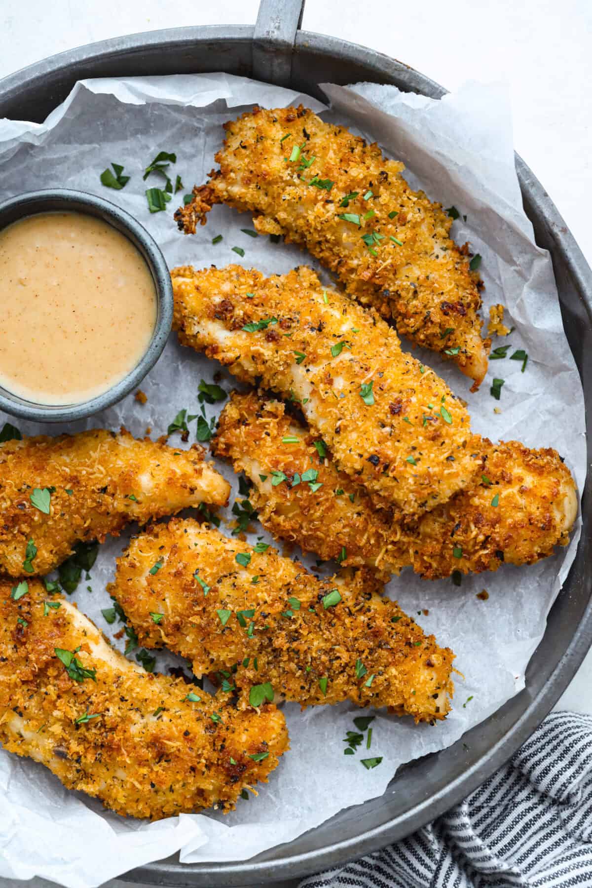 These air fryer chicken tenders are a lifesaver on crazy weeknights. Crispy, cheesy, and full of flavorโplus they cook up fast and my kidsย actuallyย ask for seconds. Total win! Overhead shot of air fryer chicken tenders on a plate next to dipping sauce.
