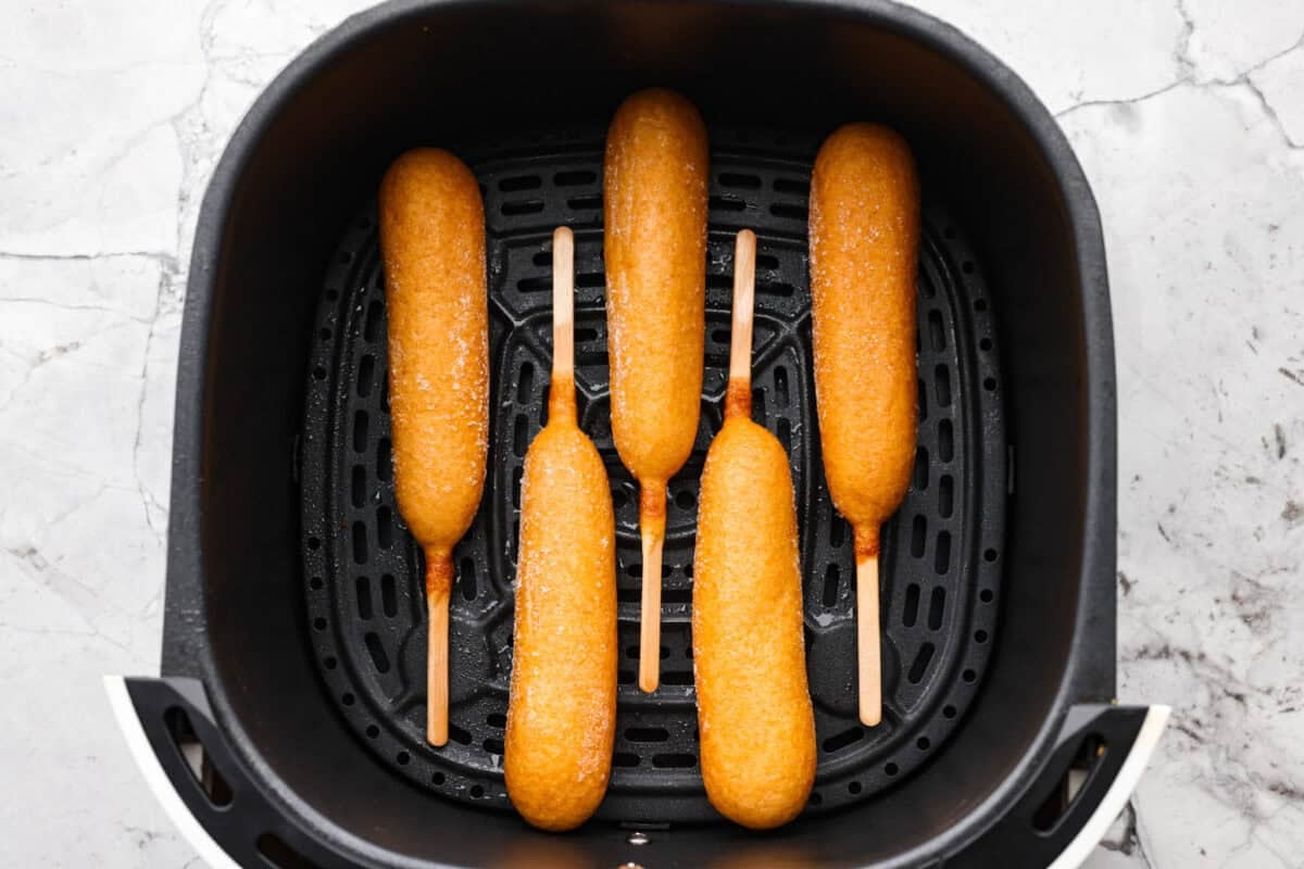 Air fryer corn dogs bring fair-style crunch without the extra oil! Crispy outside, juicy inside, and ready in minutes—perfect for a quick snack or easy meal! Corn dogs arranged in the bottom of the air fryer.