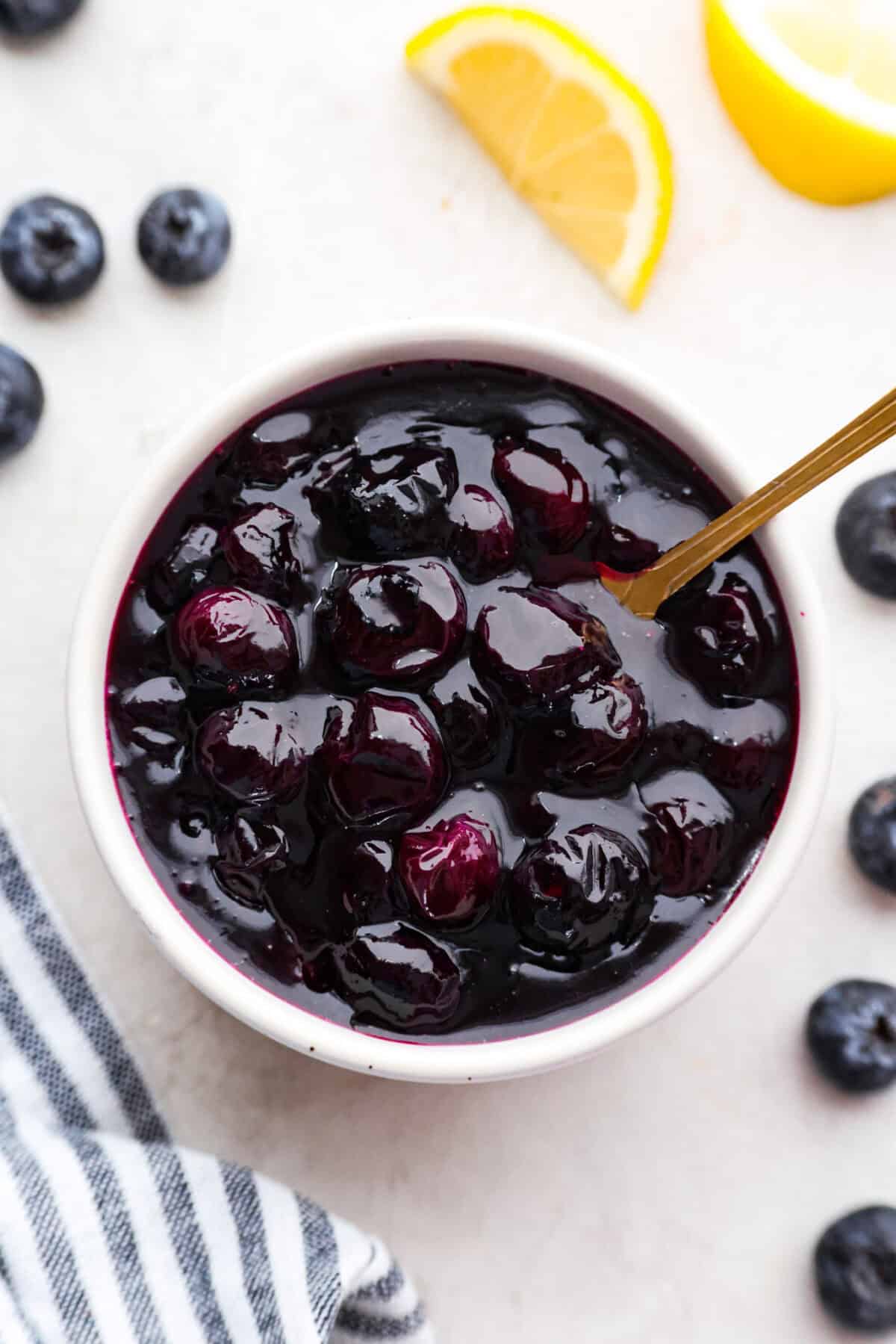Overhead shot of homemade blueberry syrup in a jar with golden spoon sticking out. 