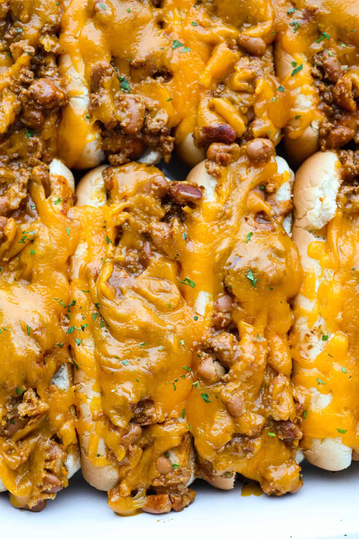 These Baked Chili Cheese Dogs are dangerously good. We’re talking soft buns, hearty chili, and ooey gooey cheese. They’re quick, messy (in the best way), and totally delicious! Close up picture of the baked chili cheese dogs.