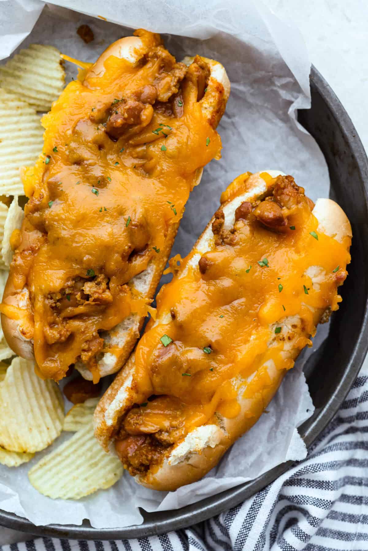 These Baked Chili Cheese Dogs are dangerously good. We’re talking soft buns, hearty chili, and ooey gooey cheese. They’re quick, messy (in the best way), and totally delicious! Overhead shot of plated baked chili cheese dogs.