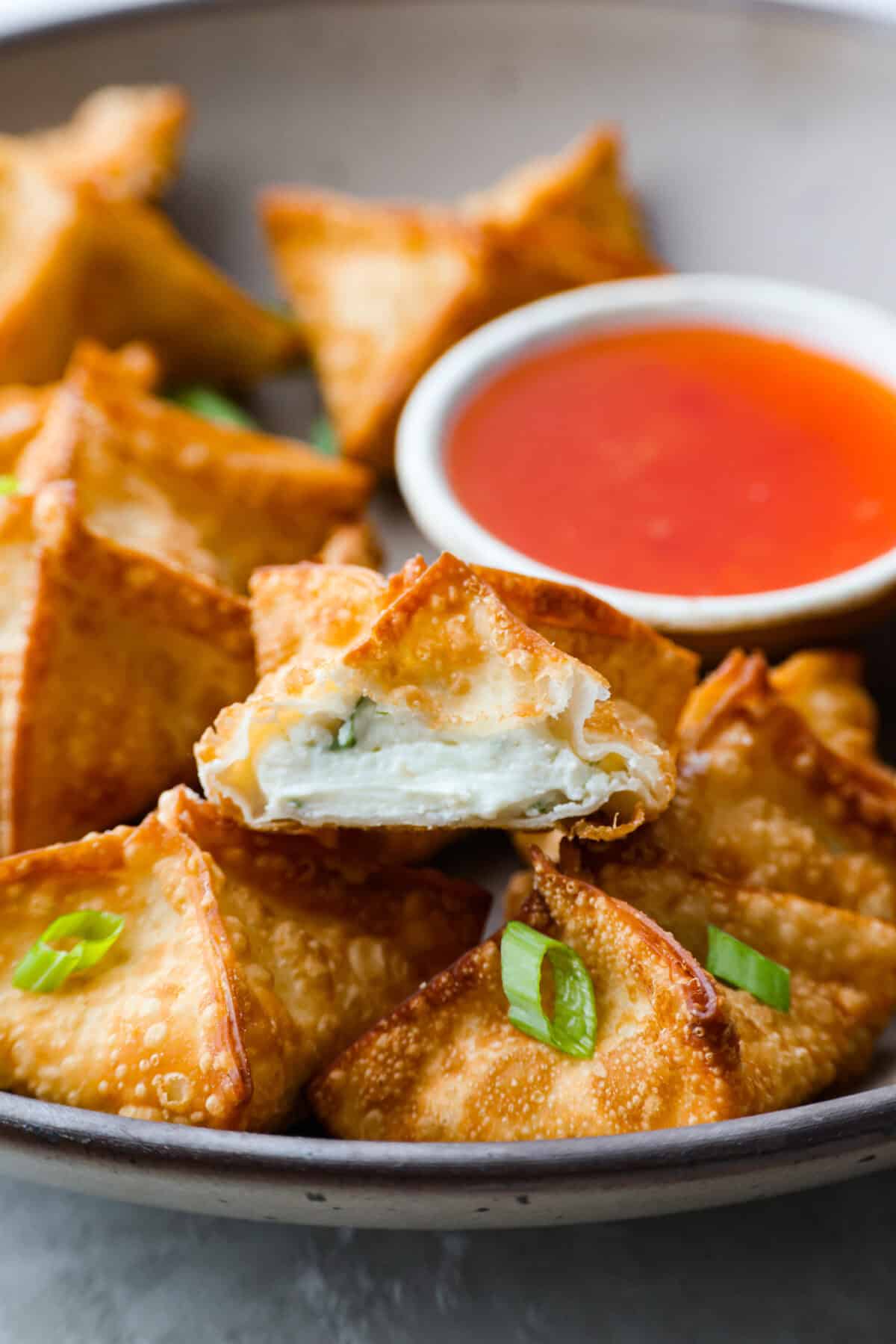 If you guys are as obsessed with cream cheese wontons as I am, you are going to love this easy-to-follow recipe! These crispy, creamy, wontons are totally doable! Close up shot of a cream cheese wonton cut in half.