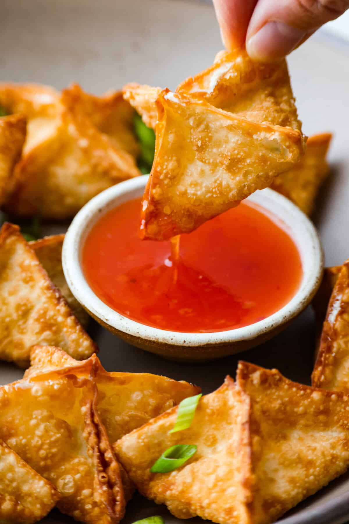 If you guys are as obsessed with cream cheese wontons as I am, you are going to love this easy-to-follow recipe! These crispy, creamy, wontons are totally doable! Cream cheese wonton being dipped in the sweet and sour sauce.