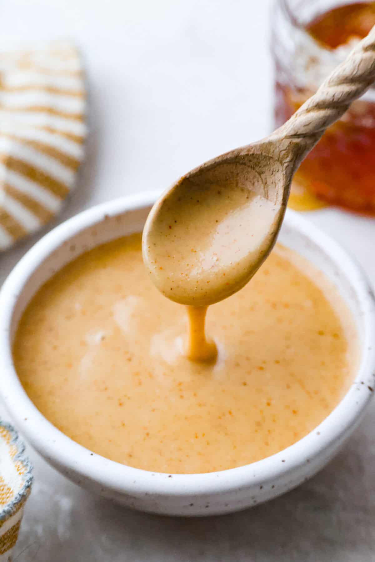 Spoon dripping honey mustard sauce above the bowl. 