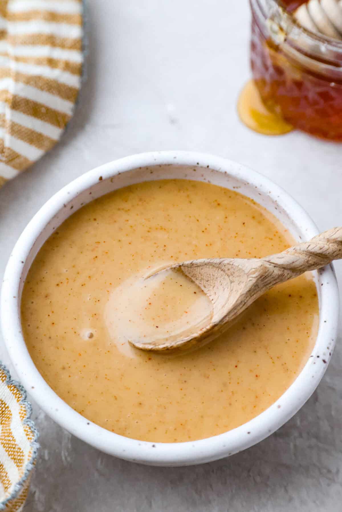 My all-time favorite sauce! This Honey Mustard is so addictive, youโll be drizzling it on everything! And the best part? It only takes 5 minutes with ingredients you probably already have in your kitchen. Bowl of honey mustard sauce with a small wooden spoon on top.