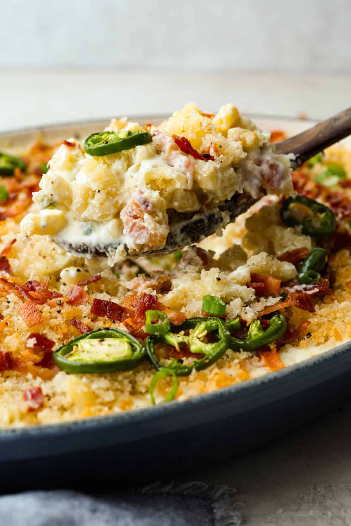 You guys, this Jalapeño Popper Mac and Cheese is downright sinful in the best way. Creamy, cheesy, spicy, and loaded with comfort food goodness! It’s easy to put together, and trust me, it’s so worth it! Side shot of someone taking a scoop of jalapeno mac and cheese out of the baking dish.