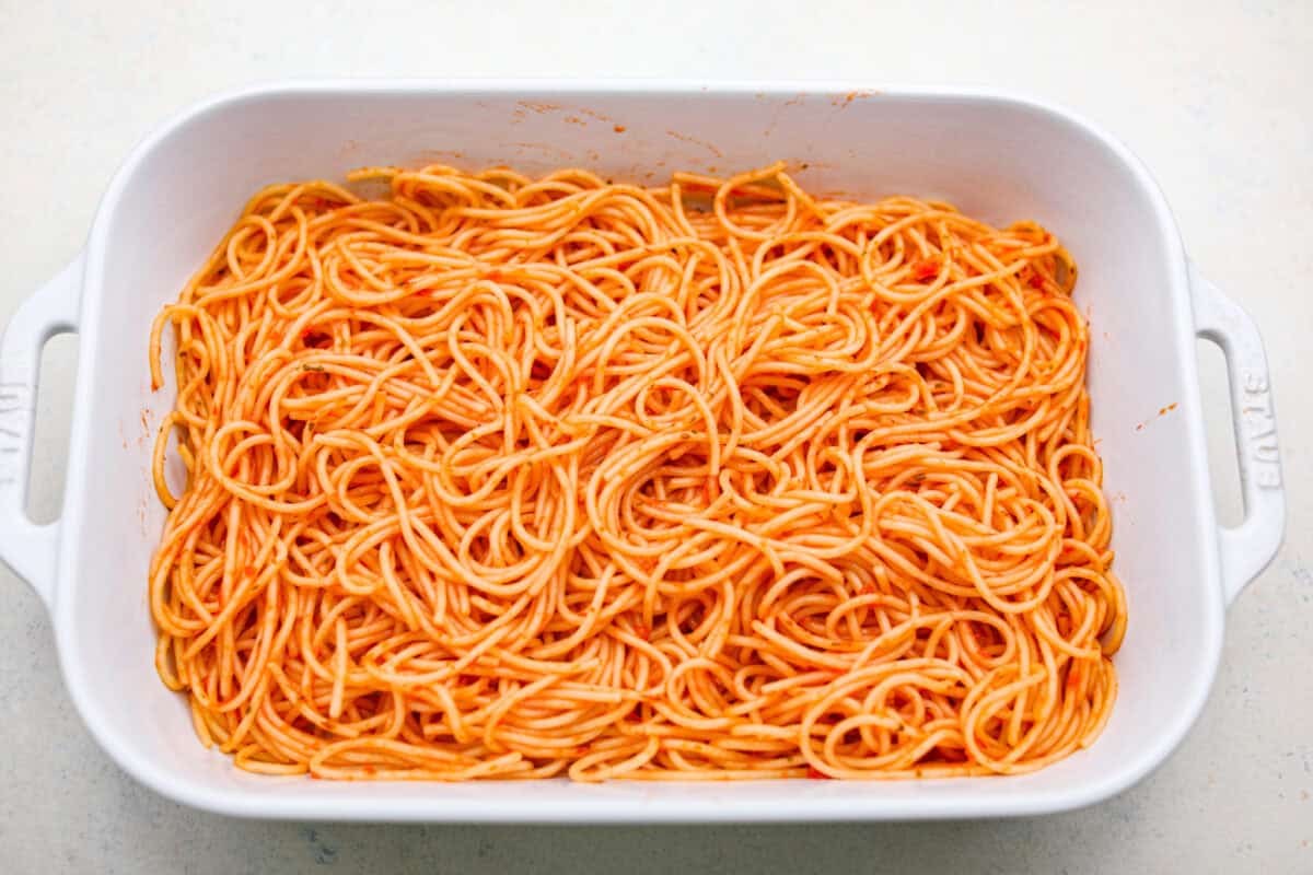 Million Dollar Spaghetti takes baked spaghetti to a whole new level. That cheesy, cream cheese, sour cream, and ricotta layer makes it so dreamy! One bite and you’ll ask, “Wait... why have I not been making spaghetti like this my whole life?” Cooked spaghetti noodles covered in marinara sauce in the bottom of a baking dish.