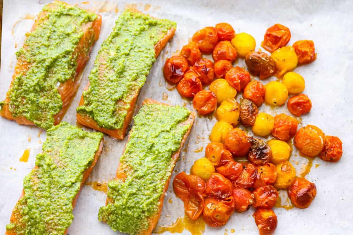 Pesto Salmon is everything. Itโs one of the easiest, lightest, most flavor-packed dinners Iโve ever made! It uses just 6 ingredients, takes 30 minutes, and it looks like you totally have your life together (even if you donโt;). Cooked cherry tomatoes next to salmon fillets covered in pesto.