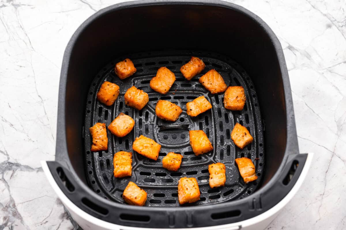 My air fryer salmon rice bowl combines crisp salmon, fluffy rice, fresh veggies, and a spicy sriracha mayo drizzle. Plus, it's ready in less than 20 minutes! Seasoned salmon pieces in the bottom of the air fryer basket.