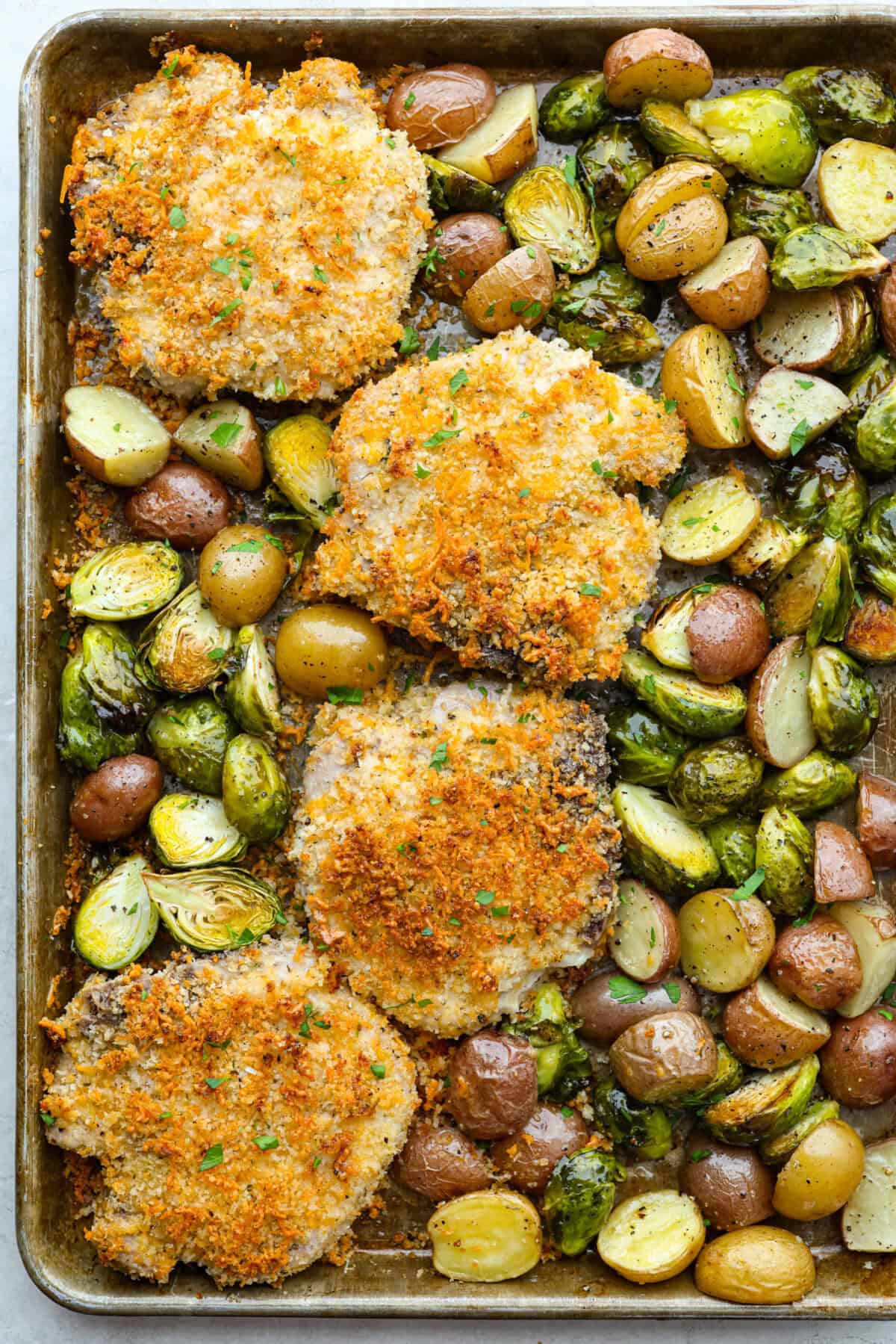 If you're looking for a tasty spin on pork chops, this is it! The crispy, cheesy texture -ย don't even get me started! YUM! Add in some roasted veggies, and you have the best Sheet Pan Crispy Pork Chops dinner! Overhead shot of cooked crispy sheet pan pork chops with potatoes and Brussels sprouts.