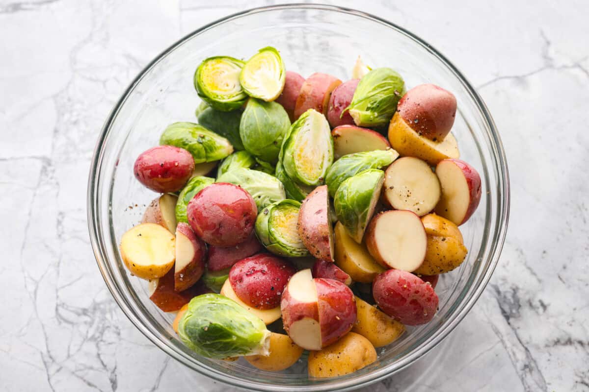 If you're looking for a tasty spin on pork chops, this is it! The crispy, cheesy texture -ย don't even get me started! YUM! Add in some roasted veggies, and you have the best Sheet Pan Crispy Pork Chops dinner! Bowl of oiled and seasoned Brussels sprouts and baby potatoes.