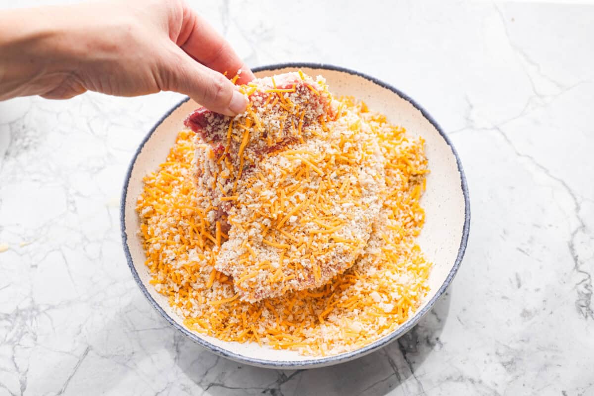 If you're looking for a tasty spin on pork chops, this is it! The crispy, cheesy texture -ย don't even get me started! YUM! Add in some roasted veggies, and you have the best Sheet Pan Crispy Pork Chops dinner! Someone dipping the dredged pork chop into the breadcrumb mixture.