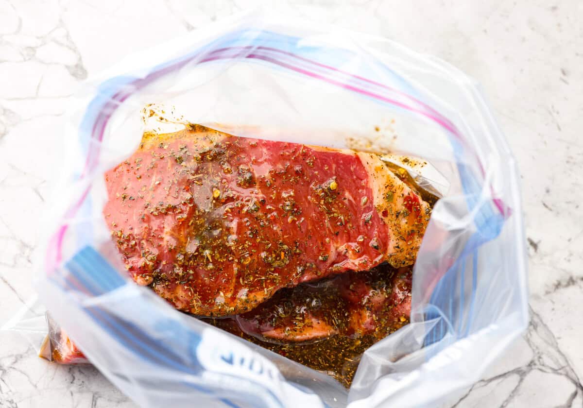 This steak marinade is one of the top recipes on my site! Itโs my go-to for turning tough, budget-friendly cuts into juicy, flavor-packed steaks that practically melt in your mouth. Overhead shot of steak covered in marinade in a zip lock bag.