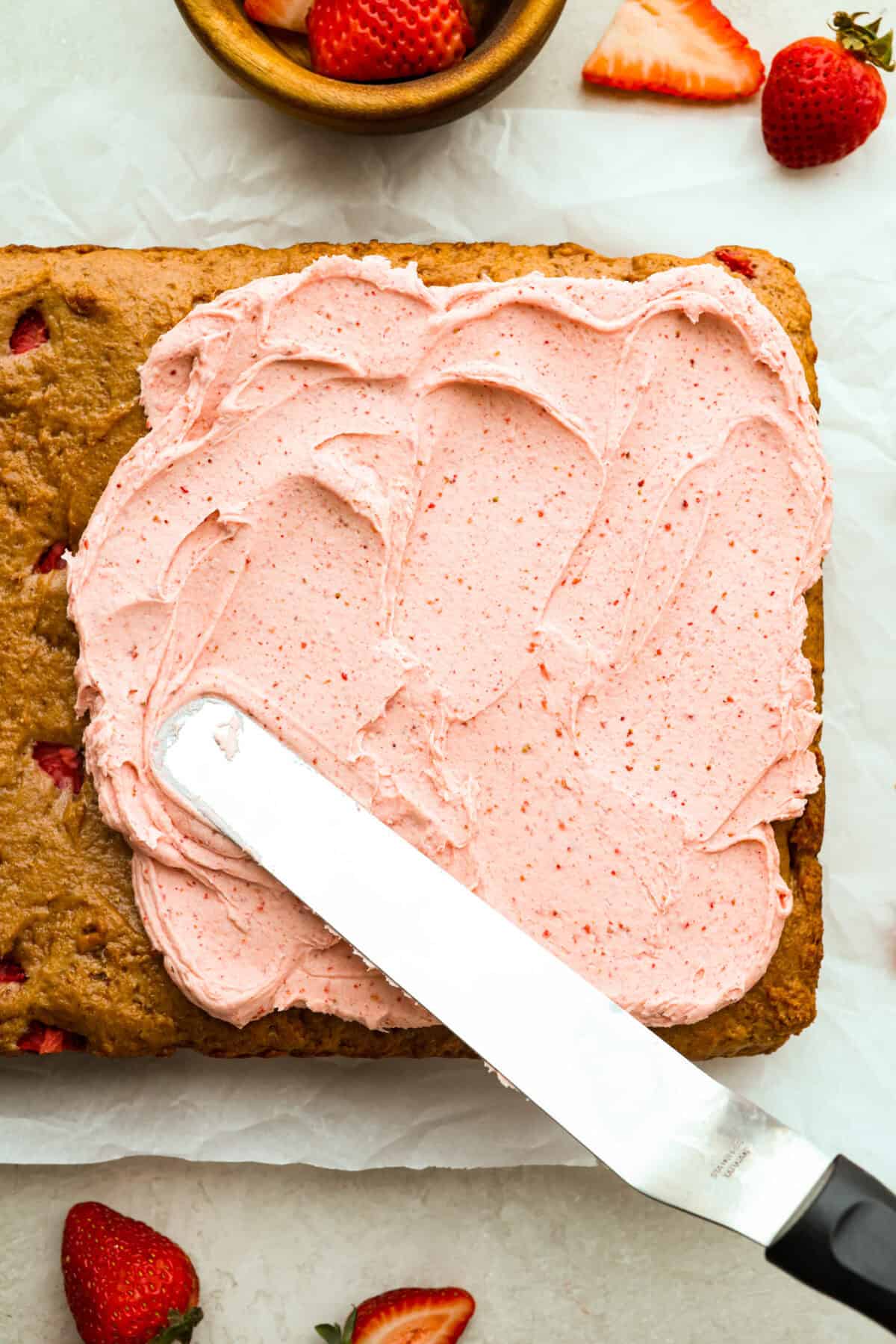 Ever since I discovered the amazing flavors that freeze-dried strawberries add, I’ve been using them as much as possible. This strawberry cake? No exception. And don’t even get me started on the frosting... It’s dangerously good. Overhead shot of someone frosting the homemade strawberry cake.