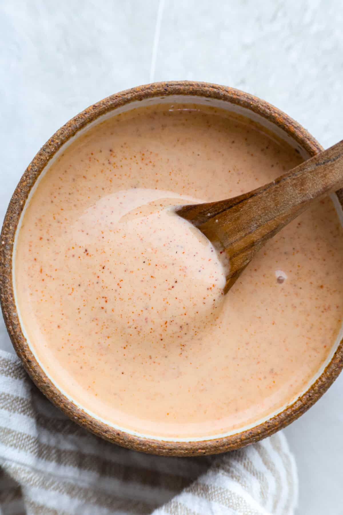 Yum Yum Sauce lives up to the name! This sweet, tangy Japanese steakhouse mayo sauce is easy to make, and you’ll want to put it on everything! Bowl of homemade yum yum sauce with small wooden spoon.