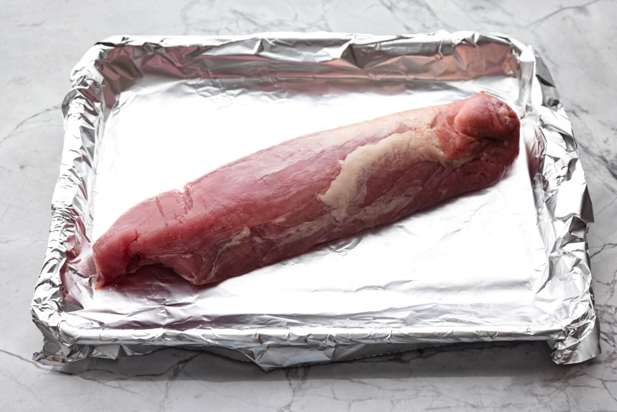 My easy Cuban sandwich is stacked with tender pork, melty Swiss, tangy pickles (my favorite), and zesty mustard! Then it's toasted in butter until perfectly crisp and golden. Overhead shot of pork on a baking sheet covered in foil.