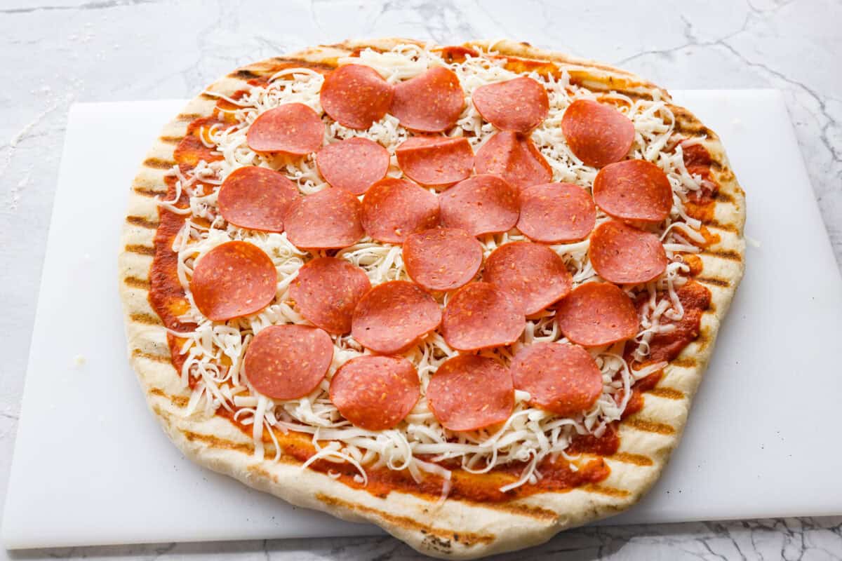 Iโm all about pizza and grilling, so when I can combine the two, itโs a win. The grill gives pizza that smoky, crispy flavor you canโt get from the oven. Trust me, this grilled pizza will have you hooked! Partially grilled pizza dough with sauce, cheese and pepperoni on it.