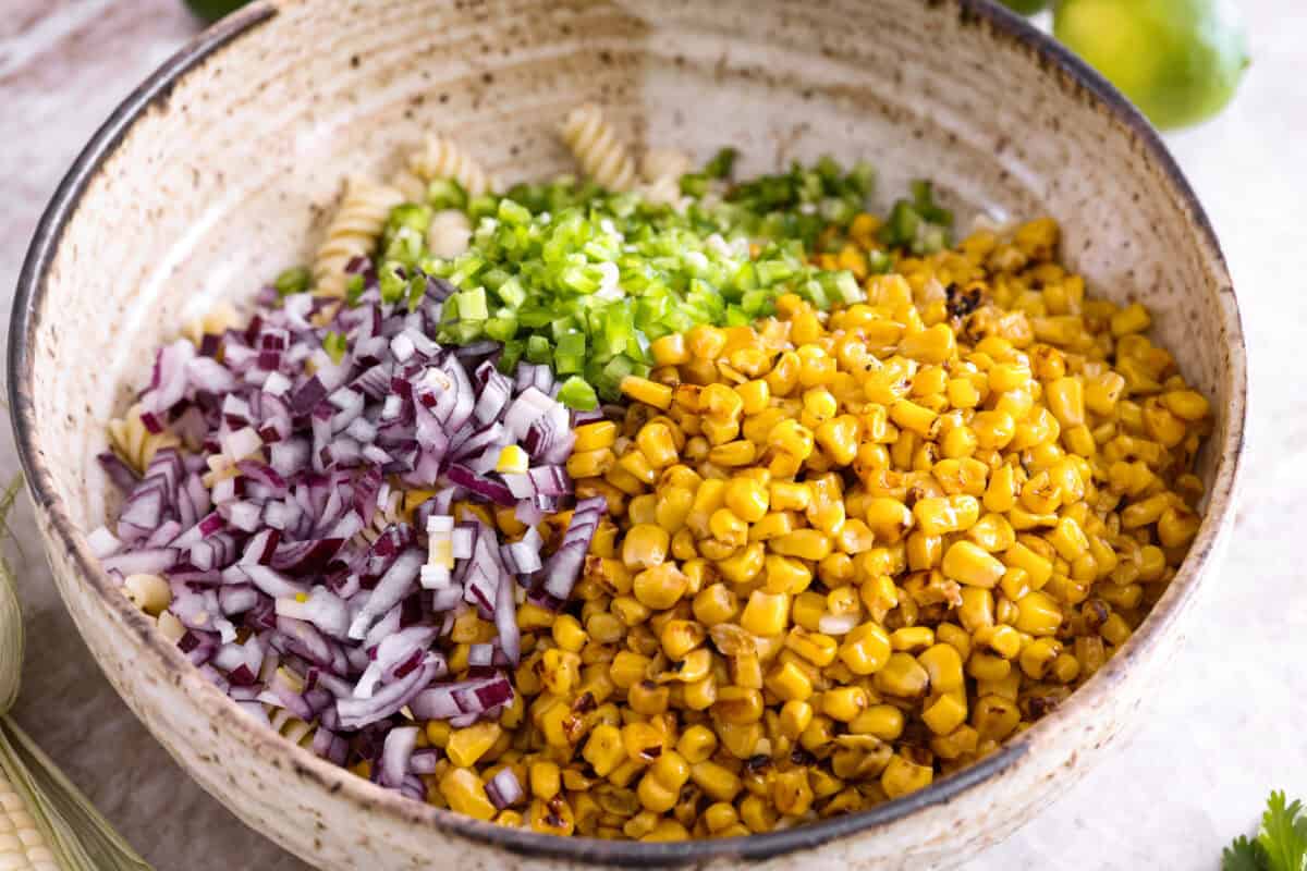 Guys, Iโm obsessed with elote, so obviously I had to turn all that smoky, creamy, cheesy, limey magic into a pasta salad big enough to feed a crowd. This oneโs guaranteed to disappear fast! Cooked pasta with diced onion, jalapeno, and corn added to it.