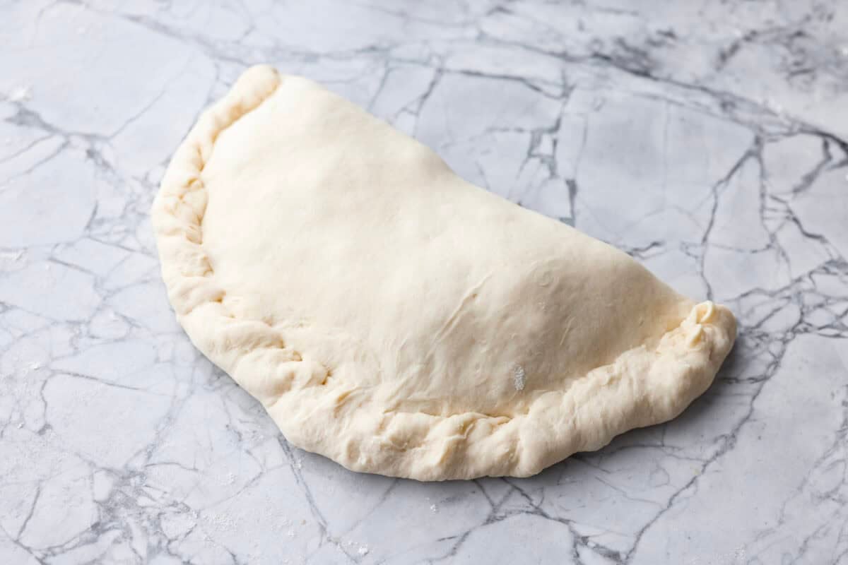 Why make calzones instead of pizza? Sometimes you just want all the pizza vibes without the mess. Calzones are like little pizza presents, warm, cheesy, and you get to make them your way! Dough circle folded in half and sealed.