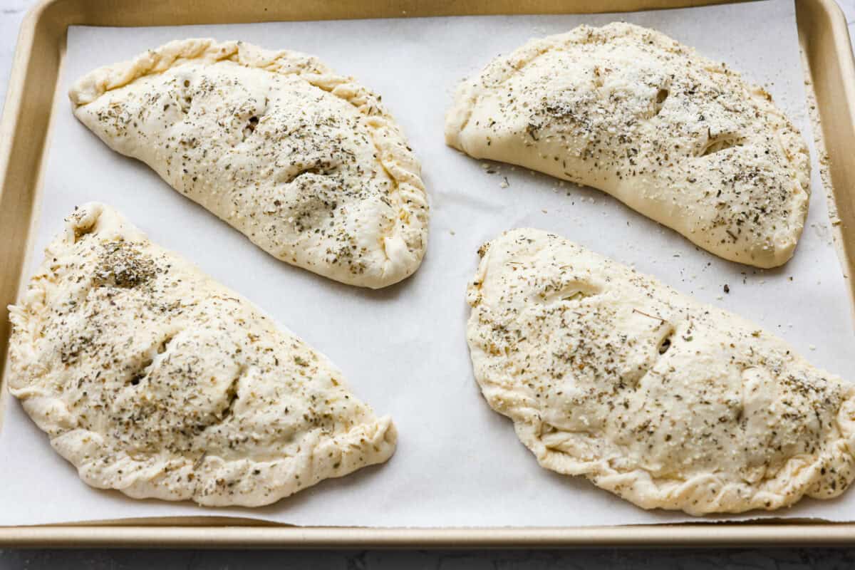 Why make calzones instead of pizza? Sometimes you just want all the pizza vibes without the mess. Calzones are like little pizza presents, warm, cheesy, and you get to make them your way! 4 calzones with slits in the top ready to go in the oven.