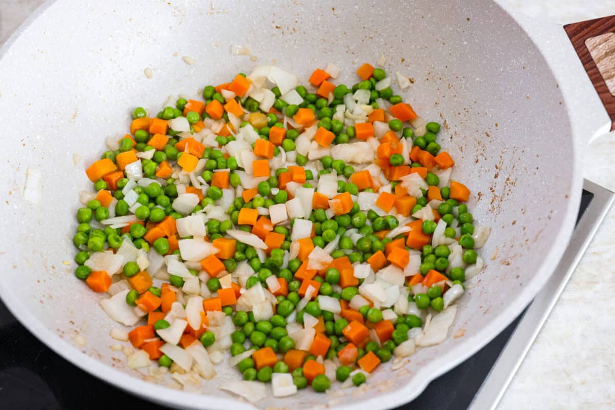 My go-to when I donโt feel like cooking? This easy chicken fried rice. I grab leftover rice and chicken, toss it all in a pan, and boom, dinner is ready in minutes. The best part? My kids devour it! Carrots, onions and peas cooking in a skillet.