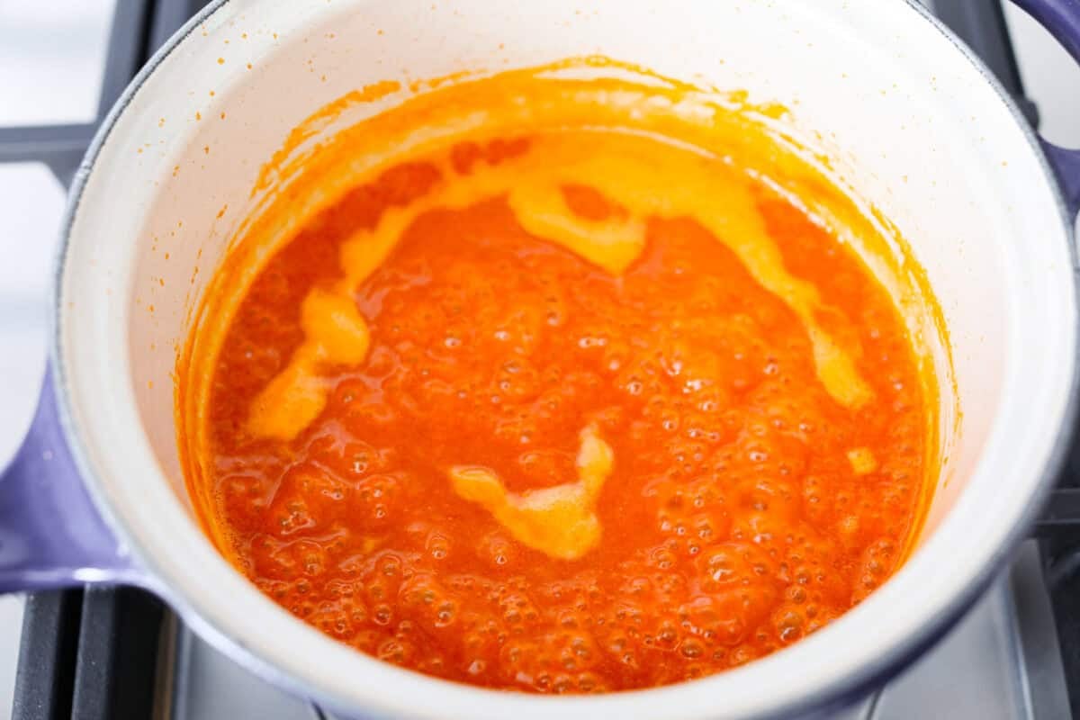 My homemade buffalo sauce is bold, tangy, and perfectly spicy! It's ready in minutes with just a few simple ingredients. Skip the store-bought stuff and make your wings, wraps, and dips next-level delicious! All of the ingredients simmering together in a pot on the stovetop.