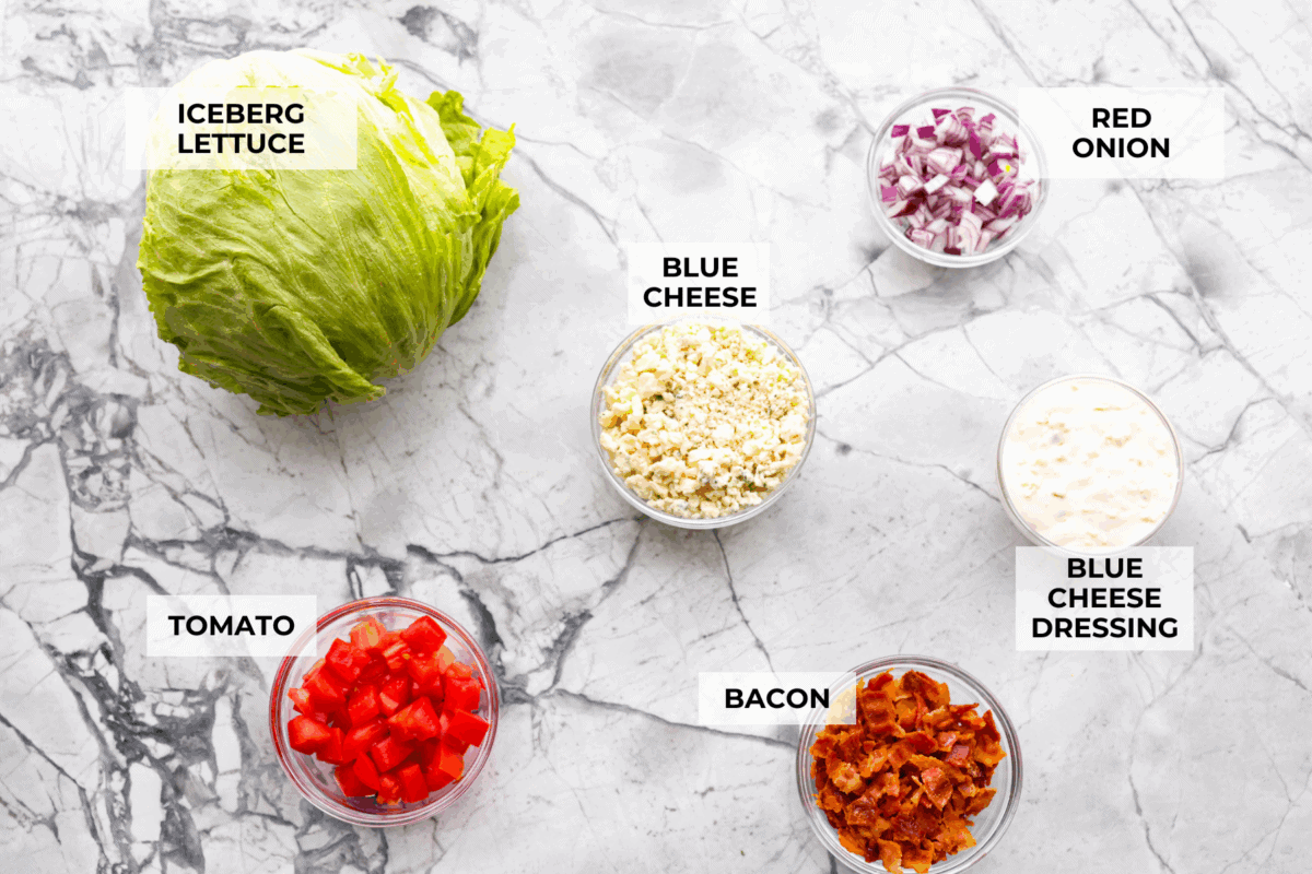 This classic wedge salad brings all the steakhouse vibes! Piled high with crispy bacon, fresh tomatoes, and a drizzle of creamy blue cheese dressing, it's a simple side that goes with just about anything. Overhead shot of labeled ingredients.