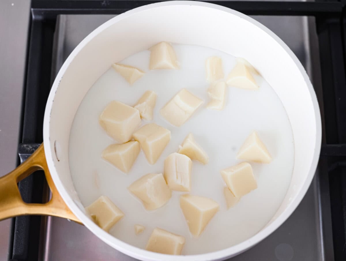My Queso Blanco is creamy, dreamy, and seriously so addictive. The secret? White American cheese! It melts like a dream, gives you that ultra-smooth texture! White American cheese chunks in milk in a pot on the stove.