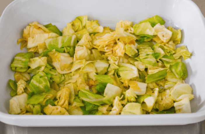 Cooked cabbage in the bottom of a baking dish.