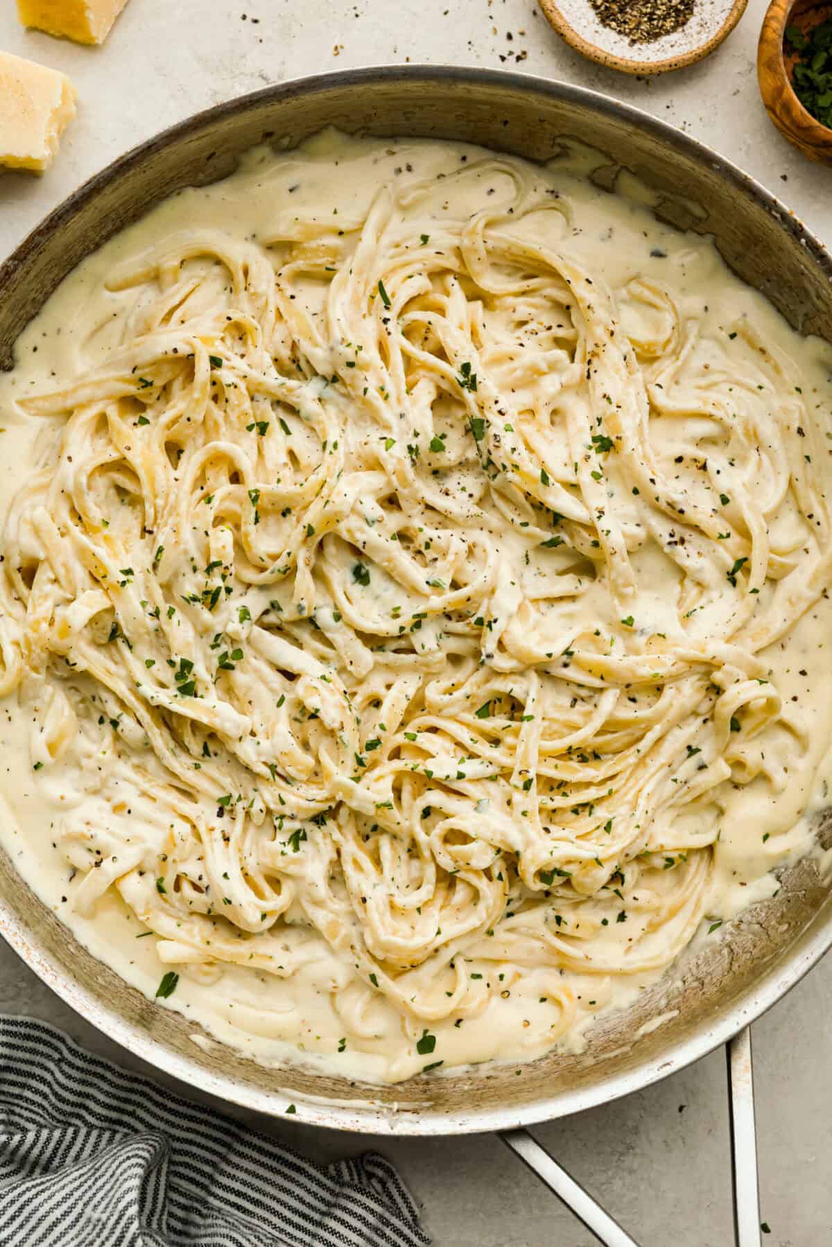 Pan of creamy Alfredo sauce with cooked fettuccini noodles. 