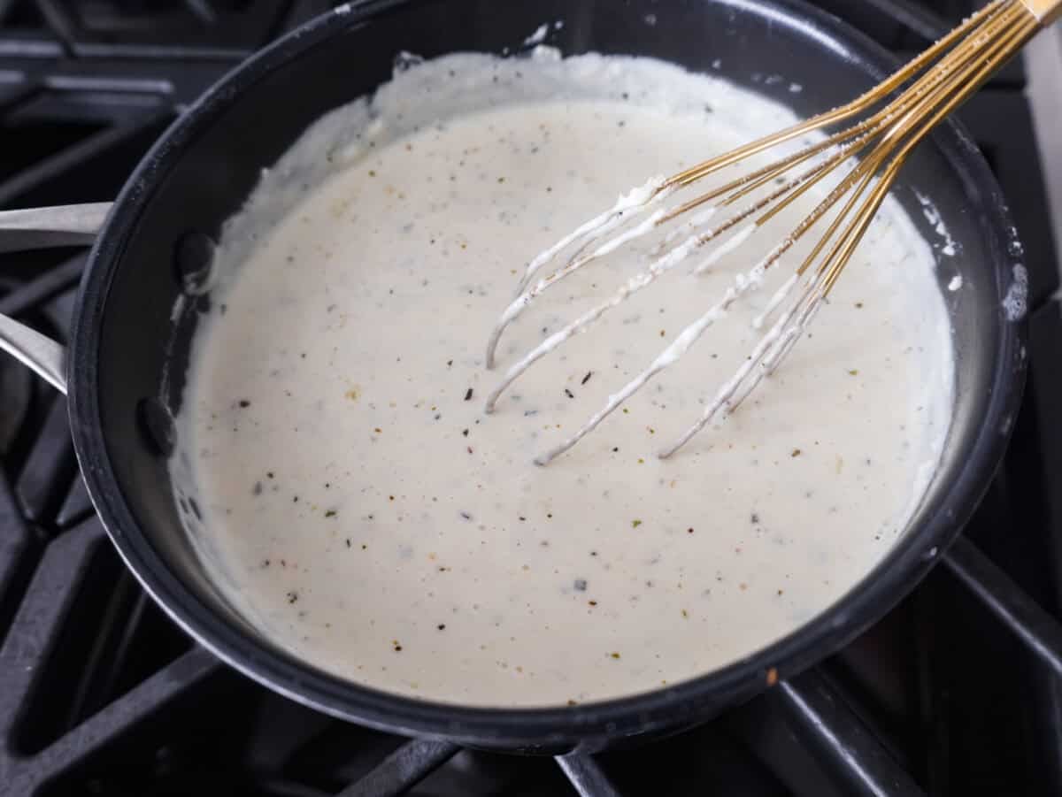 Alfredo sauce is one of my most popular recipes EVER! The secret is a little cream cheese, and ohhh my gosh, the tangy creaminess takes it to the next level. You and your kids will inhale it, I promise! Someone whisking everything together in the pan.