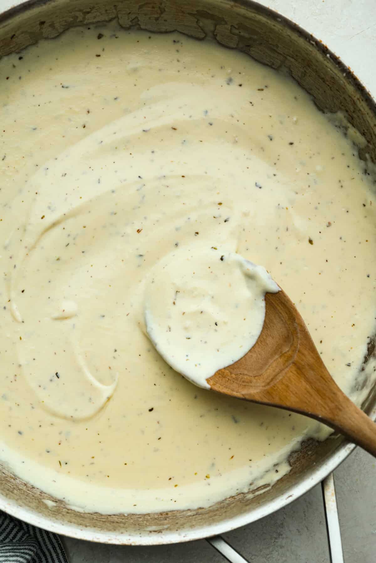 This Alfredo sauce is ultra creamy and belongs on everything. It's one of my most popular recipes EVER! It's so much better than store-bought and only takes 20 minutes to make! Pan of homemade Alfredo sauce with a wooden spoon.