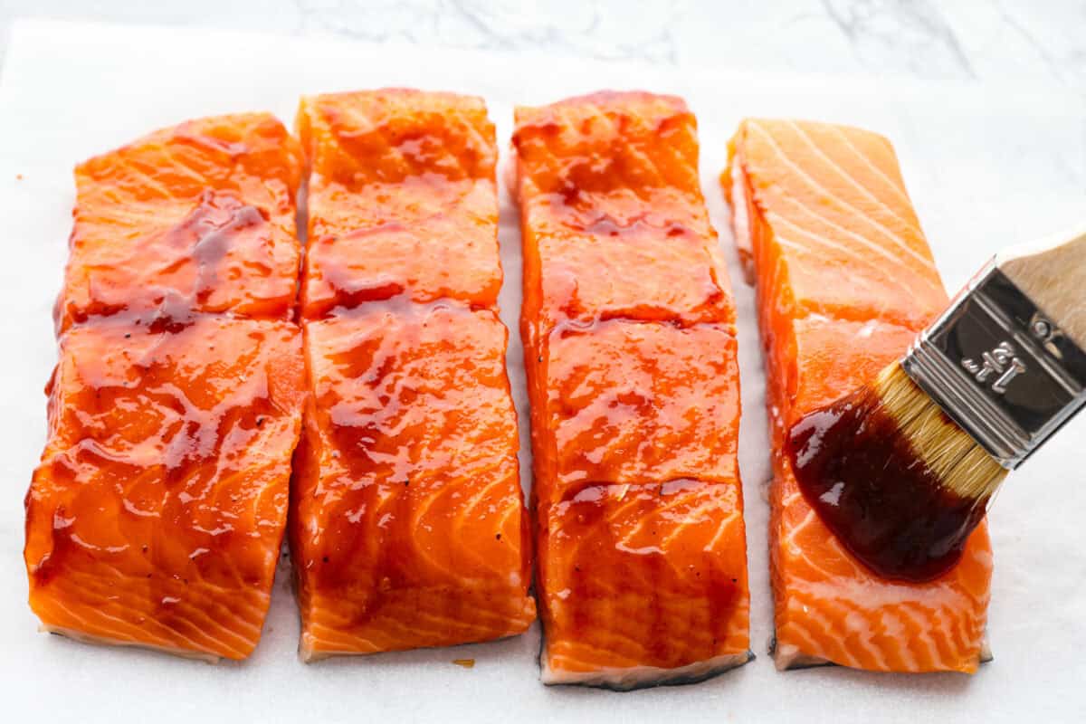 You guys know I'm obsessed with salmon! This BBQ salmon is perfectly smoky, tender, and coated in my mouthwatering homemade barbecue sauce. Someone spreading BBQ sauce on salmon filets.