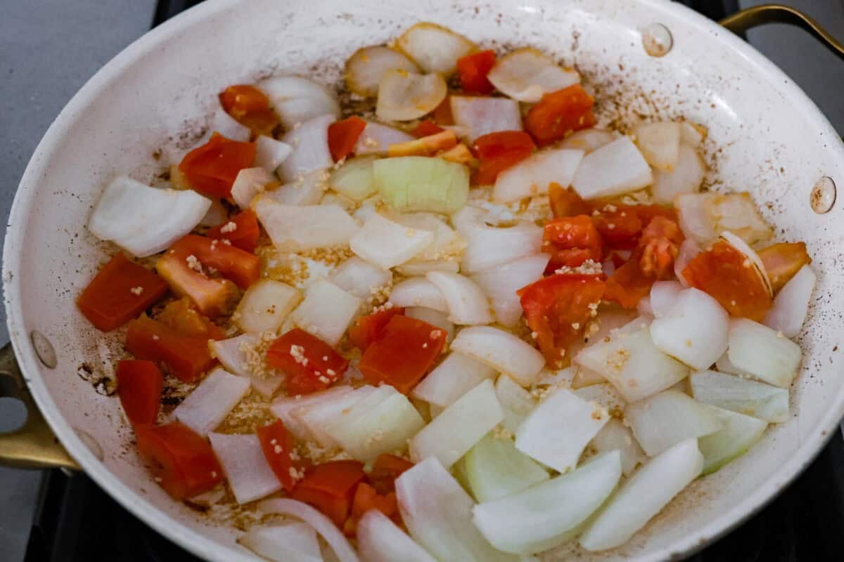 My Birria Ramen is next-level delicious! Tender shredded chuck roast, rich consommé, and slurp-worthy noodles all in one bowl. Onions, tomatoes, and garlic cooking in a skillet.