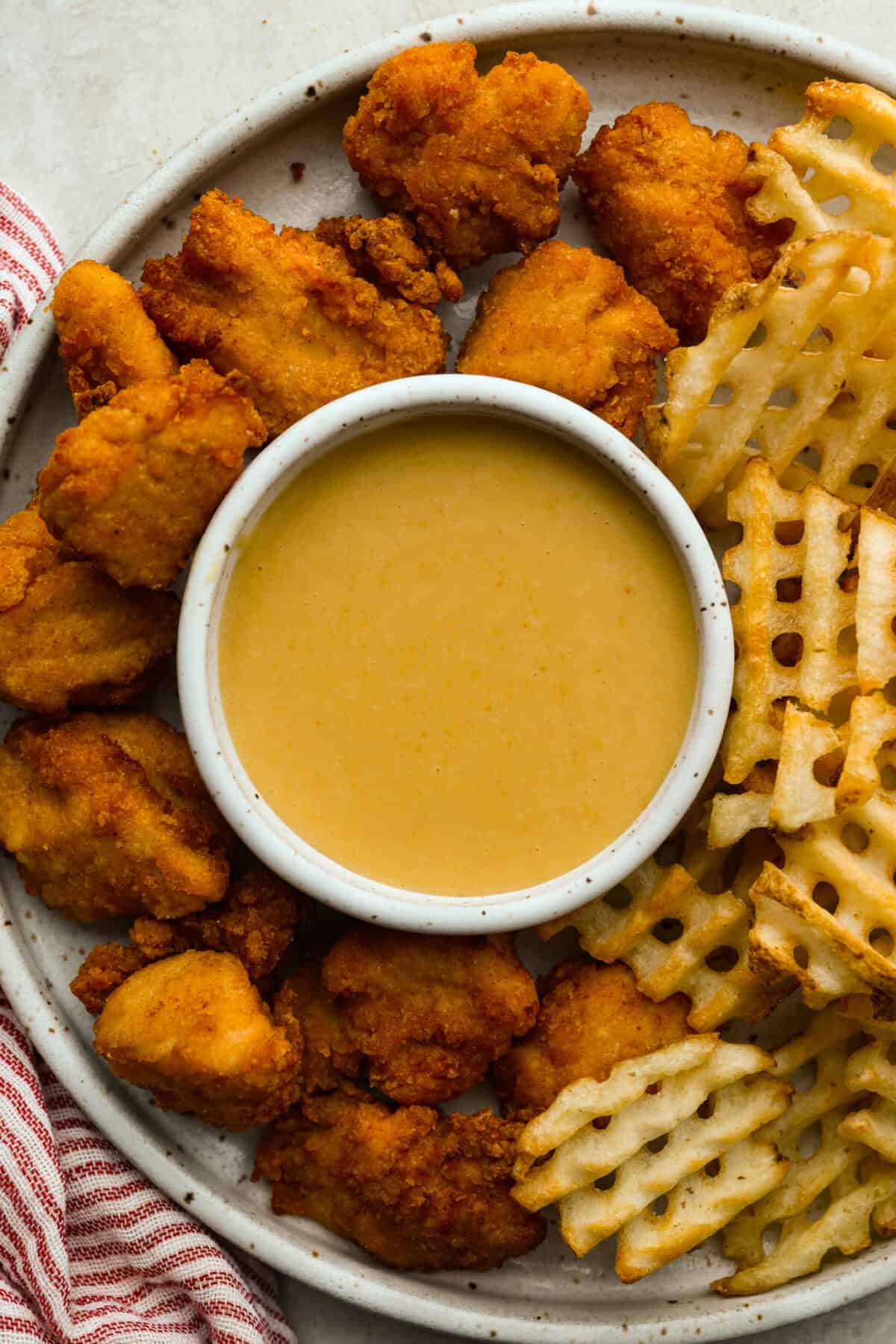 My boys were blowing through bottles of this stuff weekly. Between the price and the junk in it, I said nope and made my own Chick-fil-A Sauce. Itโs smoky, sweet, tangy, creamy magic... and honestly? Way better than the bottle. Small bowl of Chik-fil-A sauce on a plate with nuggets and fries.