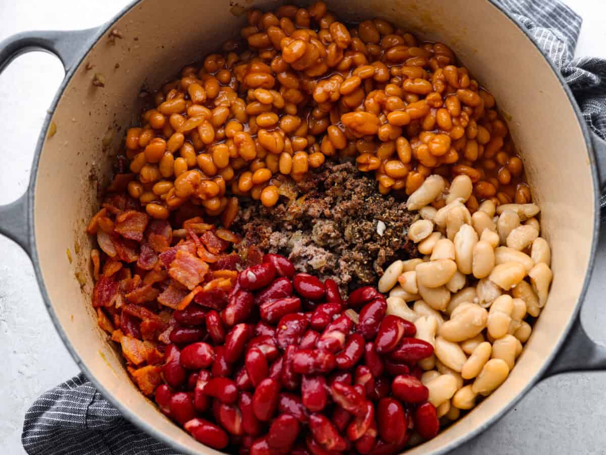 Every time I bring these cowboy beans to a summer BBQ, people start begging for the recipe, and honestly, I donโt blame them. Theyโre hearty, a little smoky, a little sweet, and always the first thing to disappear. All of the different beans added to the dutch oven with the bacon and ground beef.