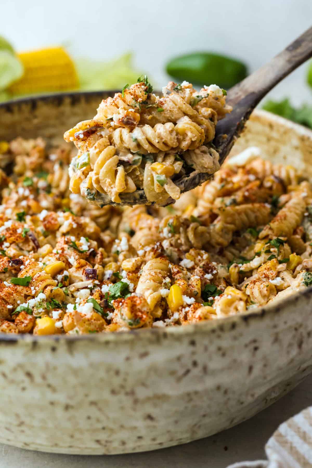 Guys, Iโm obsessed with elote, so obviously I had to turn all that smoky, creamy, cheesy, limey magic into a pasta salad big enough to feed a crowd. This oneโs guaranteed to disappear fast! Scoop of elote pasta salad being lifted from a bowl of pasta.