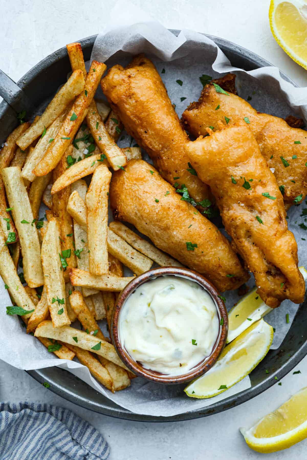 Skip the overpriced takeout and bring the pub vibes home! Crispy, golden fish and chips—light, flaky, pan-fried perfection. It’s cheaper, easier, and honestly? Way better than anything stuffed in a greasy paper bag. Plate of freshly fried fish and chips with a side of tartar sauce and lemon wedges.