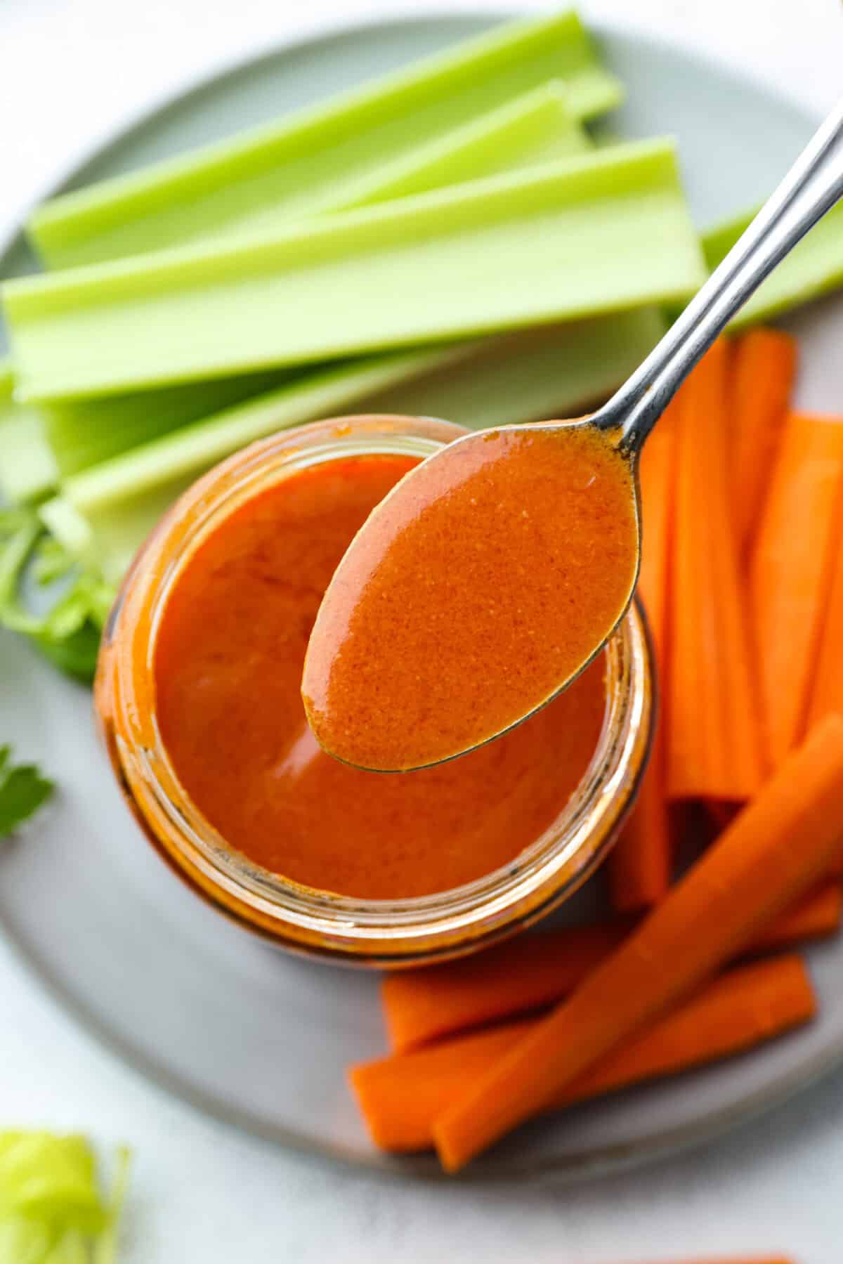 My homemade buffalo sauce is bold, tangy, and perfectly spicy! It's ready in minutes with just a few simple ingredients. Skip the store-bought stuff and make your wings, wraps, and dips next-level delicious! Overhead shot of a spoon of homemade buffalo sauce over a plate of celery and carrots.
