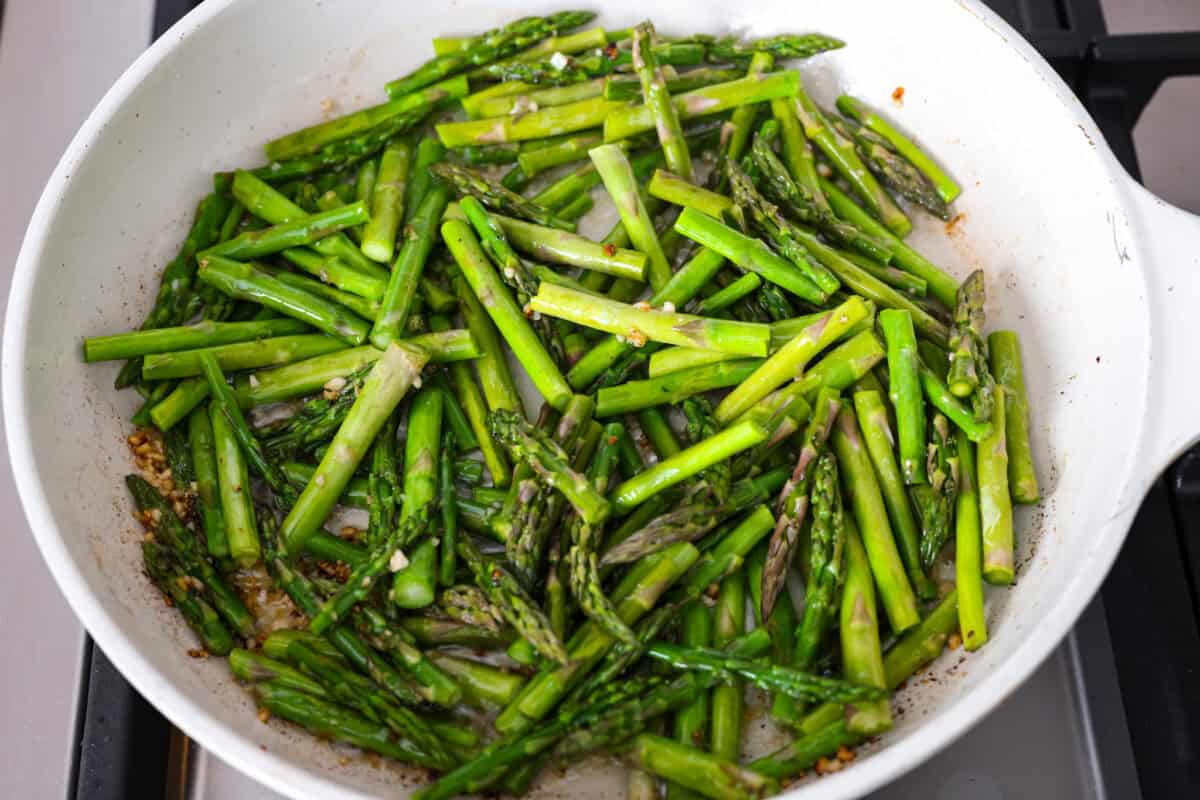 My Lemon Garlic Chicken Asparagus Pasta looks like something youโd order at a fancy bistro, but it literally takes 30 minutes! Itโs zesty, garlicky, and seriously so good! Asparagus cooking in the garlic and butter in the skillet.