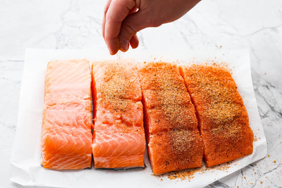 Iโm obsessed with salmon, and this Mango Salsa Salmon might just be my new favorite! Itโs super flavorful, fast to cook, and somehow my kids donโt fight me on it. That bright, juicy salsa on top? Freaking amazing. I could eat it every night! Someone sprinkling spice rub over the salmon filets.