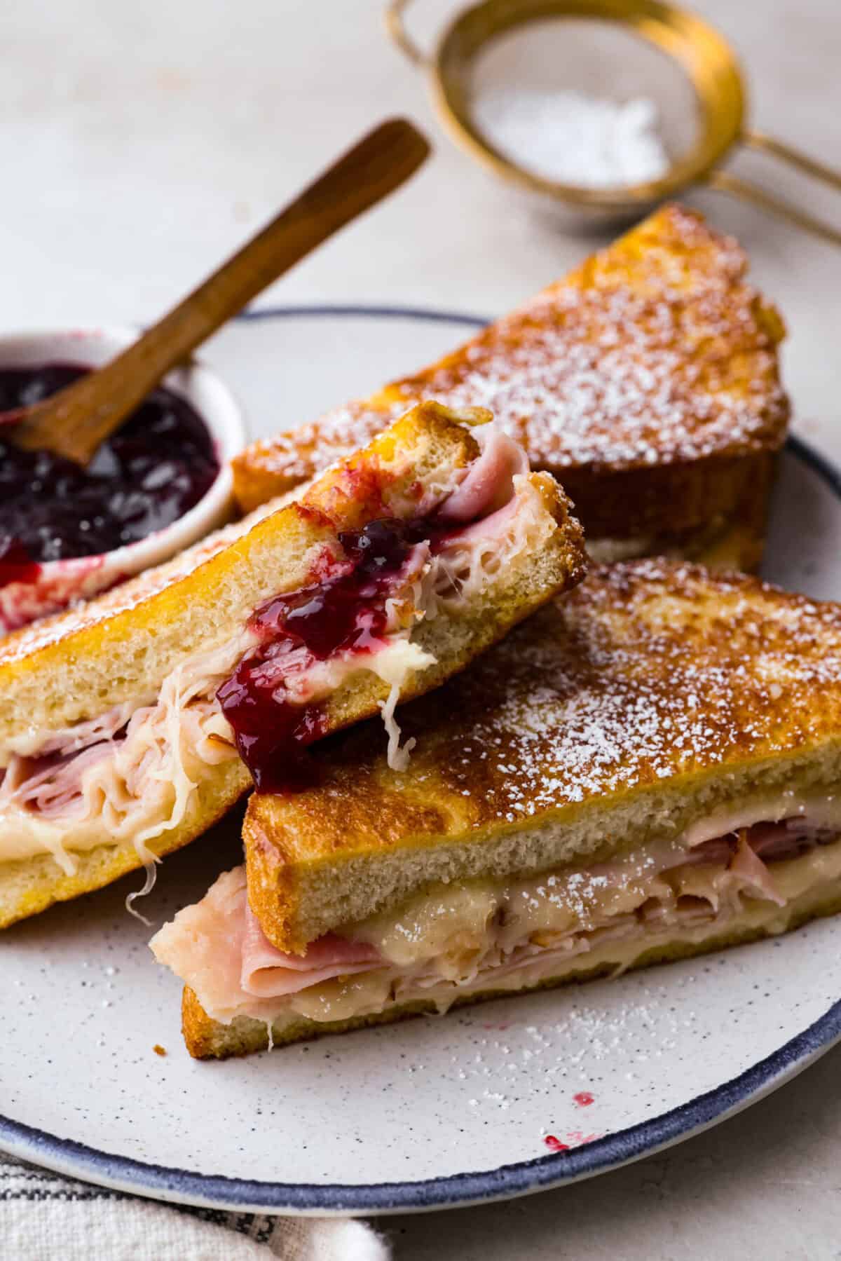 I had my first Monte Cristo sandwich at Disneyland and knew I had to recreate it at home! The melty cheese, savory ham and turkey, and golden-fried goodness deliver all the magic without the theme park ticket. Monte Cristo sliced in half on a plate with raspberry jam.