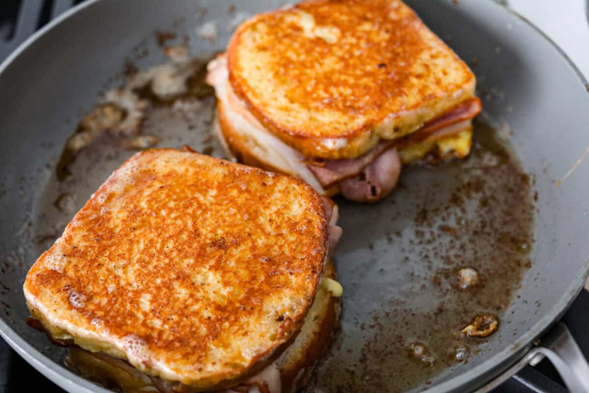 I had my first Monte Cristo sandwich at Disneyland and knew I had to recreate it at home! The melty cheese, savory ham and turkey, and golden-fried French toast bread deliver all the magic without the theme park ticket. Two Monte Cristo sandwiches toasting in the skillet.